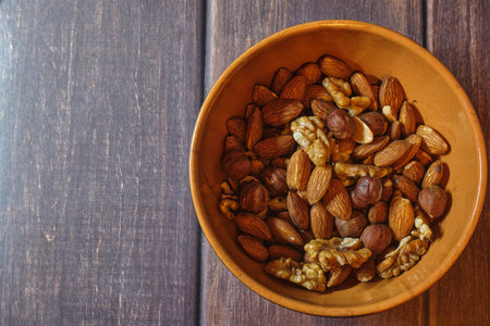 brown clay bowl with nuts: walnuts, almonds and hazelnuts on a wooden backgroundの写真素材