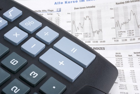 calculator on a financial newspaper showing dow jones and nasdaq graphsの写真素材