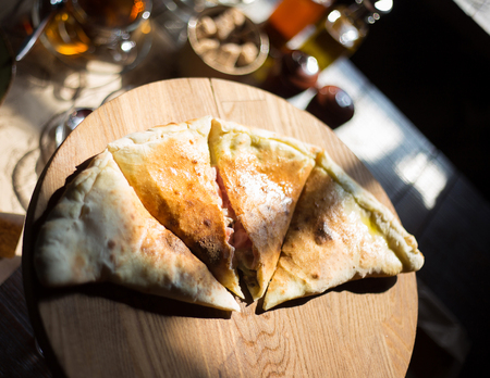 Closed pizza calzone is cut into pieces on a wooden plate