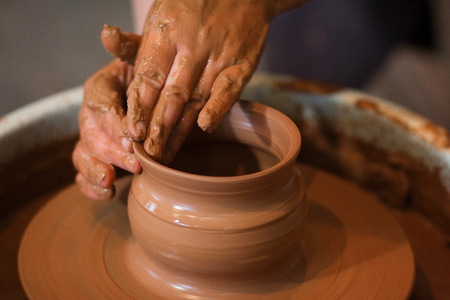 Rotating potter's wheel and clay ware on it taken from above. A sculpts his hands with a clay cup on...