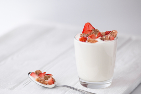 Natural yogurt  with strawberry and multigrain flakes on a white wooden table. Healthy food. Breakfast. Front viewの写真素材
