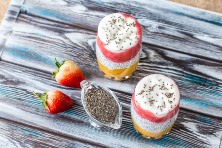 Chia pudding with mango, natural yogurt, chia, wild strawberry in a glass on a wooden table. Healthy dessert, proper nutrition, super food. Top viewの写真素材
