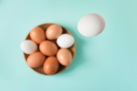 White egg falls in a wooden plate with eggs on a blue table. Happy Easter. Selective focus. Top view