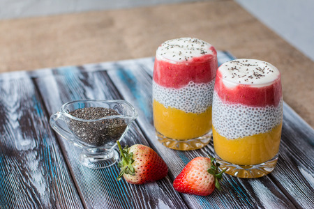 Chia pudding with mango, natural yogurt, chia, wild strawberry in a glass on a wooden table. Healthy dessert, proper nutrition, super food. Front viewの写真素材