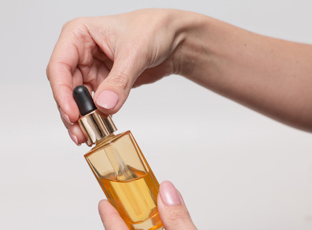 Pipette bottle with cosmetic oil in female hand on a light background . Skin care product. Health...