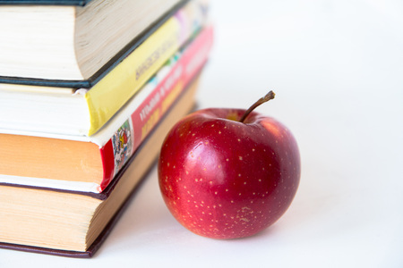 Red mature juicy apple near books. On a white table. Front viewの写真素材