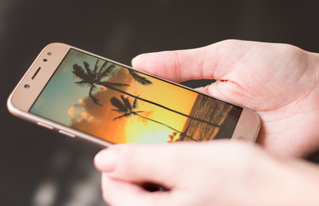 The hand of the woman holds phone with the photo of the place of a dreamの写真素材