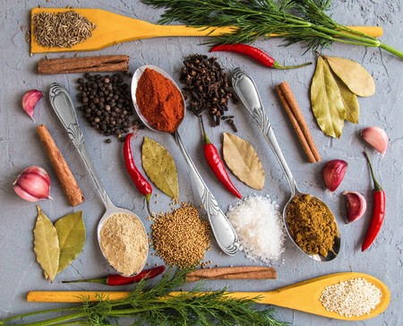 Different spices in wooden and metall spoons on grey background. Bay leaf. Garlic. Fennel. Mustard seeds. Zira. Red pepper. Ginger root. Black pepper. Carnation. Pepper pods. Cinnamon. Salt. Sesame seed.の写真素材