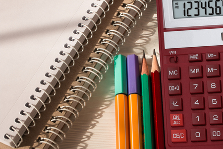 Colored pencils, desktop calculator and notebooks on white wooden table.  School and office supplies. Close up. Top viewの写真素材