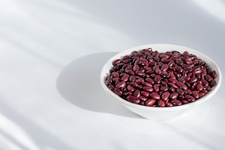 Grains of red beans in a white plate on a white table. Front viewの写真素材
