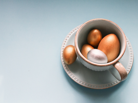 Gold  and silver Easter eggs in a porcelain mug on a blue background. National holiday celebration concepts. Happy Easter. Close up. Top view. Copy space.の写真素材