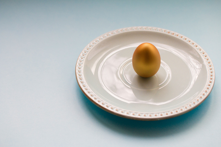 Golden Easter egg on a porcelain saucer against a blue background. National holiday celebration concepts. Happy Easter. Front view. Copy spaceの写真素材
