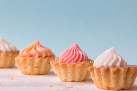 Small cakes with cream on a white table on a blue background. Selective focus. Front view.の写真素材