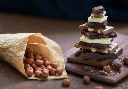 The different grades of chocolate put by the hill on a wooden board, with a filbert can on a rusty metal surface. Nuts and sweets. Front view. Selective focus.の写真素材