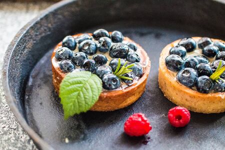 Delicious blueberry tartalets with vanilla cream and fresh raspberry berries on a black cast iron...