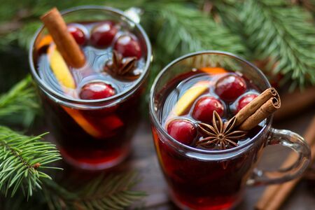 Mulled wine in glass mug with berries, cinnamon sticks and star anise on brown wood table with fir-tree branches. Traditional Christmas hot drink. Top view.の写真素材