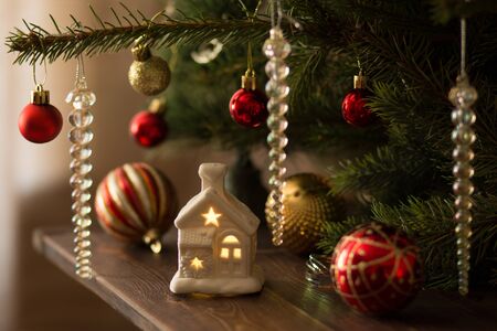 Toy decorative little house on wood brown table under the Christmas Green Tree decorated with tree...