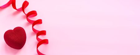 Valentines day concept. Banner with red velvet heart shaped cake on pink background with red velvet ribbon.  Sweet present. A symbol of love happiness and devotion. Top view.  Copy spaceの写真素材