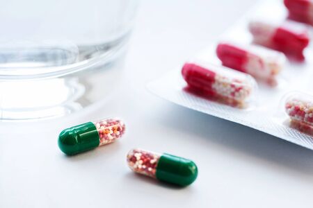 Capsules in blister with water in a clear glass cup on a grey surface. Medicine concept. Macro. Front view. Copy spaceの写真素材