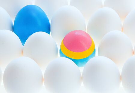 One Multicolored and one blue egg among many white eggs Preparation for coloring at Easter. Copyspace. Front view.の写真素材