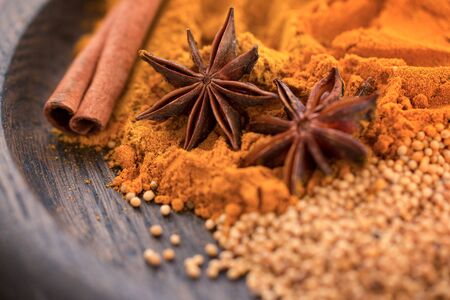 Different spices. Cinnamon sticks, star anise, mustard seeds and turmeric powder on a wooden plate. Close-up.  Macroの写真素材