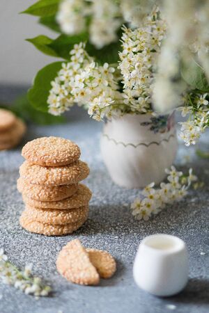 Freshly baked round sesame cookies with a bouquet of bird cherry on a gray table. Cook at home. Light background, beautiful decor. Selective focus. Front viewの写真素材