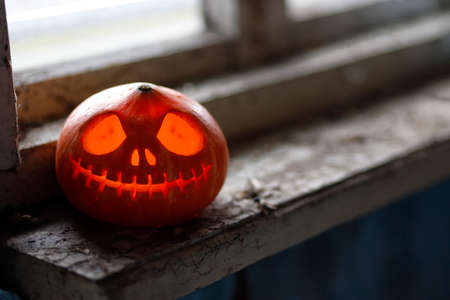 Halloween pumpkin on the dirty window sill of an old house window. Big spooky helloween symbol. Selective focusの写真素材