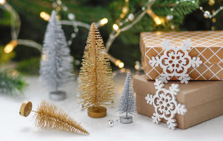 Christmas presents and gift boxes wrapped in kraft paper on a wooden table with gold and silver decorative Christmas trees, fir-tree branches, and decoration. New Year, Christmas concept.の写真素材