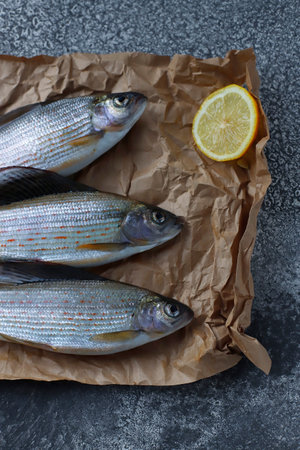 Freshly caught grayling with lemon slices is on parchment paper on the table. Freshwater fish. Preparation for cooking. Top viewの写真素材