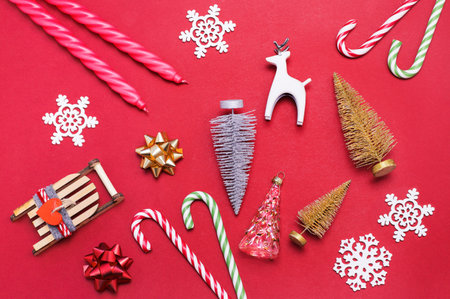 Gold and silver decorative Christmas tree and sled, candy canes, candles and snowflakes on a red background. Christmas gift preparing. Christmas decor. New Year and Christmas concept. Flat lay.の写真素材