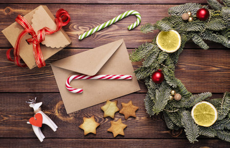 Christmas wreath, gift, coffee mug with marshmallows, envelope and homemade cookies and various Christmas decorations on the wooden table. Rustic christmas wreath, flat lay.の写真素材