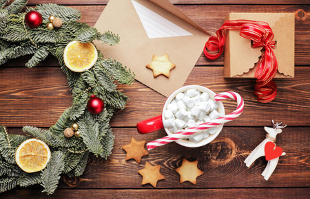 Christmas wreath, gift, coffee mug with marshmallows, envelope and homemade cookies and various Christmas decorations on the wooden table. Rustic christmas wreath, flat lay.の写真素材