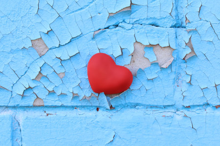 Red heart on an old cement wall with cracked blue paintの写真素材