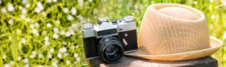 Straw hat and the retro film photo camera on a wooden chair in the summer garden.の写真素材