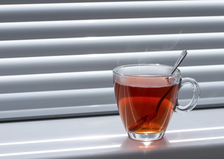 Glass mug of tea on the windowsill on the window with shuttersの写真素材