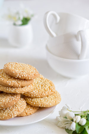 Freshly baked round sesame cookies with a apple tree flowers and three tea cups on a white table.の写真素材