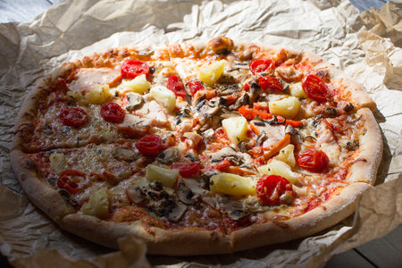 Pizza with ham, mushrooms and pineapple on a baking paper on a black tableの写真素材