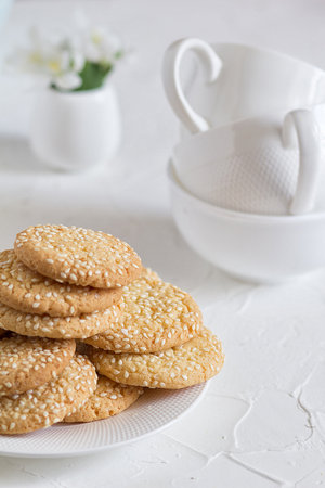 Freshly baked round sesame cookies with a apple tree flowers and three tea cups on a white table.の写真素材