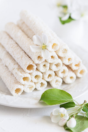 Delicate sweet cookies in the form of tubes in coconut flakes filled with vanilla cream on a white plate.の写真素材