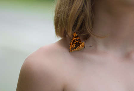 A butterfly sits on the naked shoulder of a young girl.の写真素材