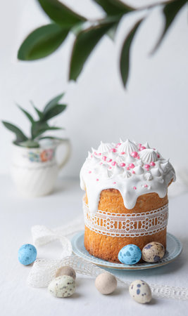 Traditional homemade Easter cake, decorated with glaze, pastry sprinkles and lace ribbon on a blue plate on a white table with colored quail eggs. Happy Easter. Front view.の写真素材