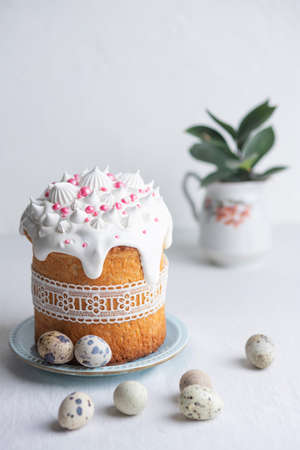 Traditional homemade Easter cake, decorated with glaze, pastry sprinkles and lace ribbon on a blue plate on a white table with quail eggs. Happy Easter. Front view.の写真素材