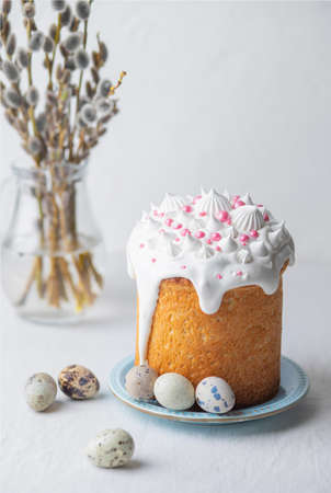 Traditional homemade Easter cake, decorated with glaze and pastry sprinkles on a blue plate on a white table with quail eggs and willow branches in the background. Happy Easter. Selective focus. Vertical photo.の写真素材