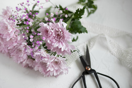 Metal antique scissors, lilac chrysanthemums and white lace ribbon on a white table.の写真素材