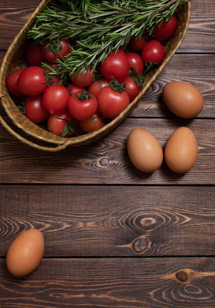Fresh tomatoes, cucumbers, a few sprigs of rosemary in a wicker basket, chicken eggs on a wooden table. Harvesting. Farm product.の写真素材