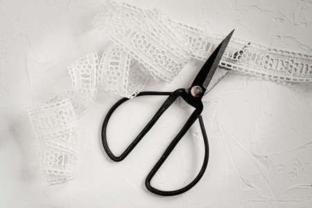 Metal antique scissors and white lace ribbon on a white table.の写真素材