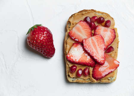 A sandwich with peanut butter, with strawberries and pomegranate seeds on a white table.の写真素材