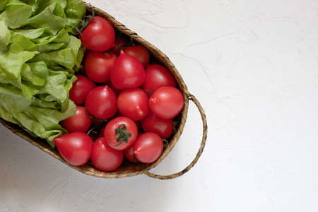 Fresh tomatoes and lettuce leaves in a wicker basket on a white surface. Harvest. Farm product.の写真素材