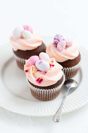 Three Easter chocolate cupcakes with caramel filling and decoration of small Easter eggs from marzipan on a white porcelain plate. Selective focusの写真素材