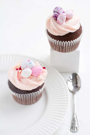 Two Easter chocolate cupcakes with caramel filling and decoration of small Easter eggs from marzipan on a white porcelain plate. Selective focusの写真素材
